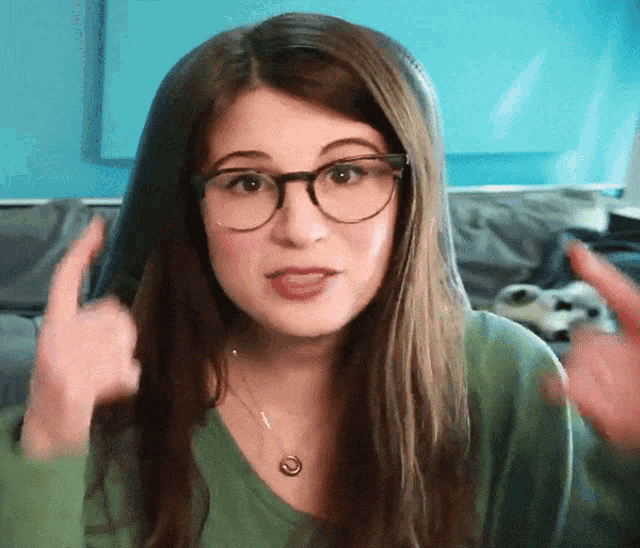 a young woman wearing glasses and a green shirt is giving a thumbs up