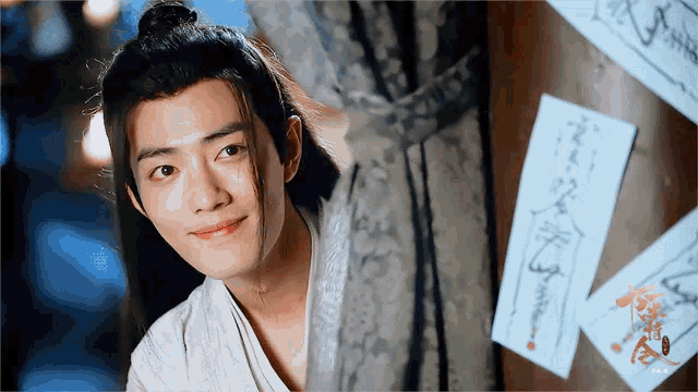 a young man with long hair is smiling while looking out a window