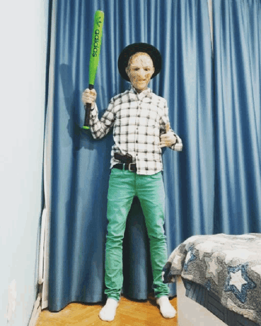 a person holding a green adidas baseball bat in front of a blue curtain
