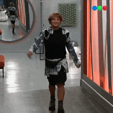 a man is dancing in a hallway while a woman walks behind him in a mirror