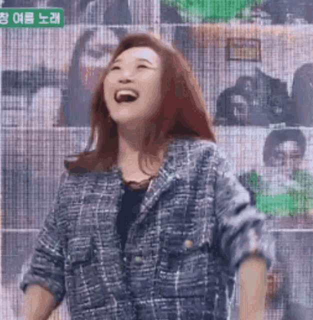 a woman in a plaid jacket is laughing in front of a screen with chinese writing on it .