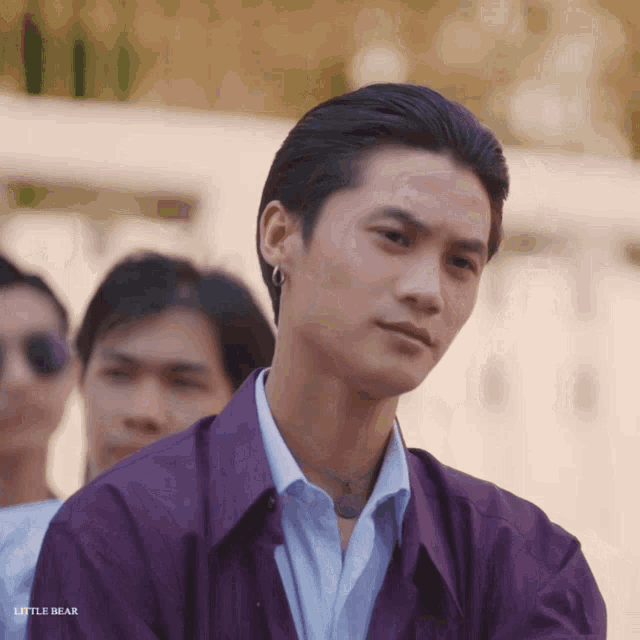 a man wearing a purple jacket and a blue shirt with the words little bear below him