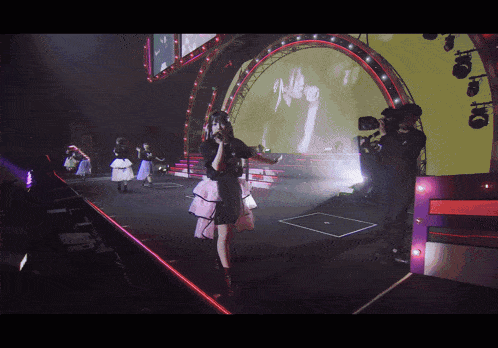 a woman singing into a microphone on a stage with a cameraman behind her