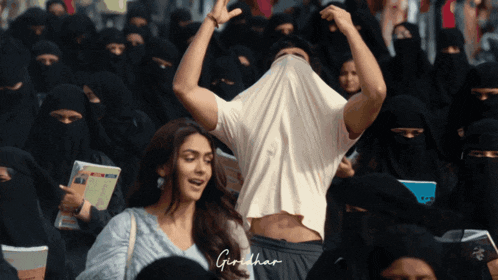 a man with his shirt covering his face stands in front of a crowd with the name girdhar written on the bottom