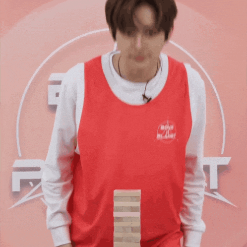a man wearing a red shirt that says boys planet is playing jenga