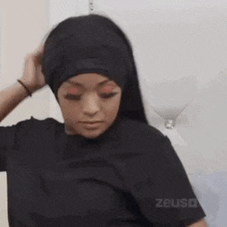 a woman wearing a black headband is sitting on a bed and touching her hair .