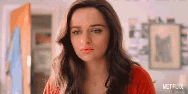 a close up of a woman 's face with a red sweater and necklace .