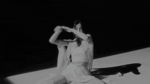 a woman in a white dress is sitting on the floor in a black and white photo .