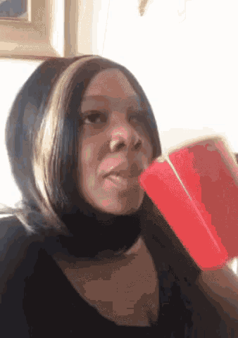 a woman drinking from a red cup while wearing a black shirt