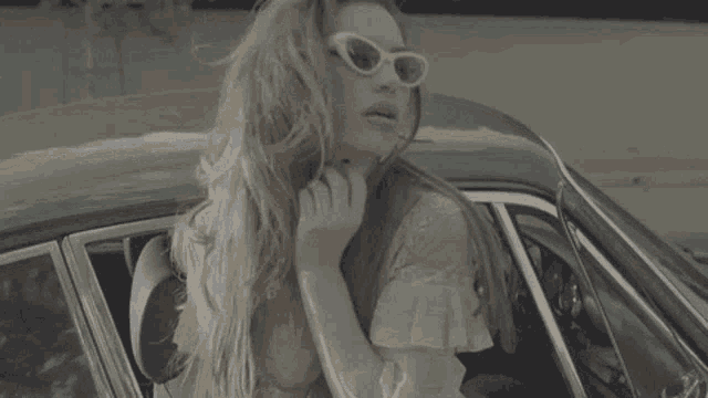 a woman is sitting in a green car wearing sunglasses