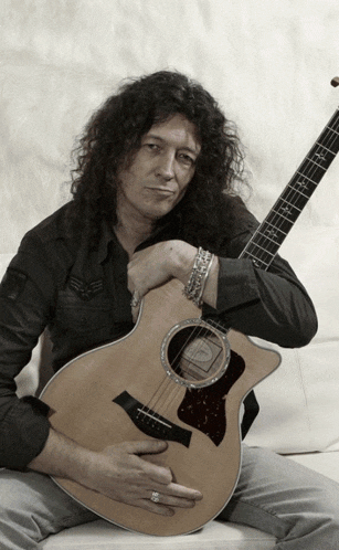 a man with long curly hair is holding a guitar with a taylor logo on it