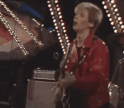 a man in a red jacket is playing a guitar on stage .