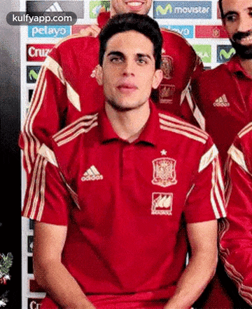 a man wearing a red adidas shirt is sitting in front of a group of men .