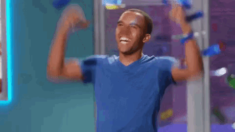 a man in a blue shirt is raising his arms in the air while confetti falls around him .