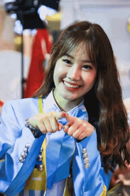 a woman in a blue jacket is smiling and making a heart shape with her hands