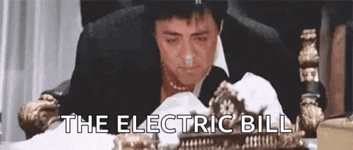 a man in a suit and tie is sitting at a table with a clock on it and the words `` the electric bill '' .