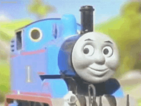 thomas the train is smiling and looking at the camera while standing next to a blue train .