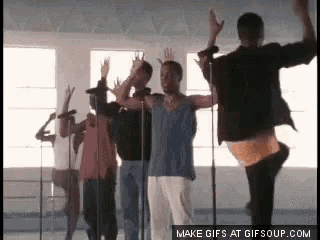 a group of people are dancing and singing in front of microphones with their hands in the air .