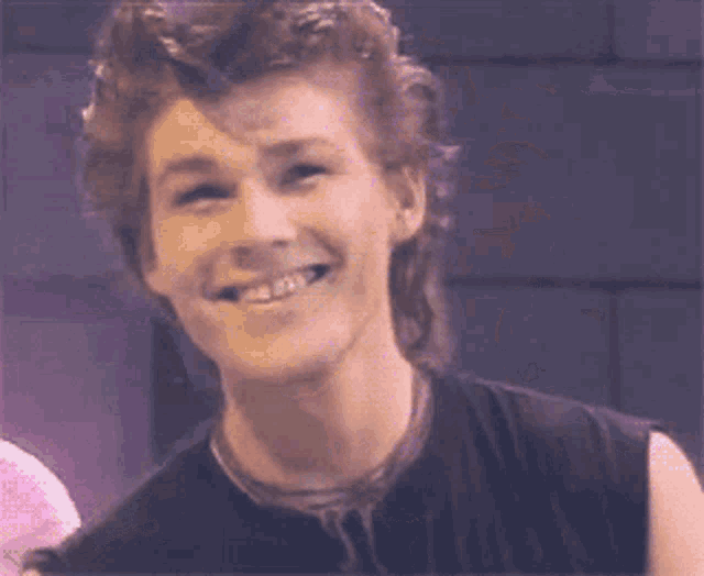 a man with a mullet is smiling and wearing a black shirt