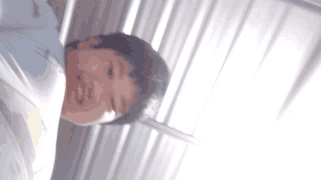 a boy in a blue shirt is smiling in front of a window