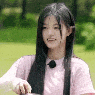 a girl with long black hair is wearing a pink shirt and holding a spoon .