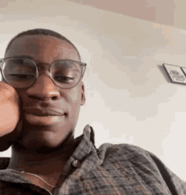 a man wearing glasses and a plaid shirt is sitting in a room .