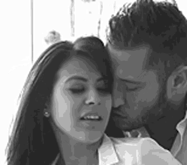 a black and white photo of a man kissing a woman on the cheek .