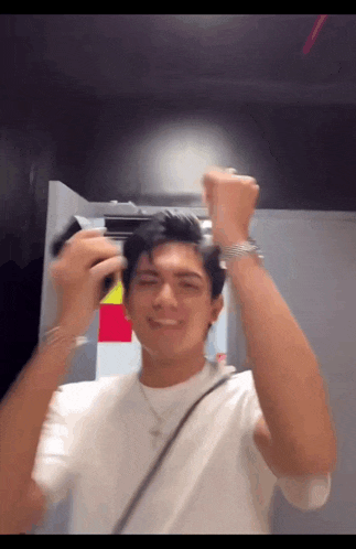 a man wearing a white shirt and a necklace is holding a gun to his head .