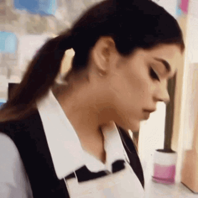 a woman wearing a white shirt and a black vest is standing in front of a table .