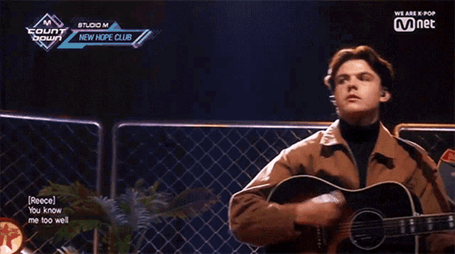 a man singing into a microphone while holding a guitar in front of a fence that says interstate on it
