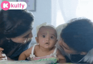 a woman and a man are playing with a baby on a bed and the baby is looking at the camera .