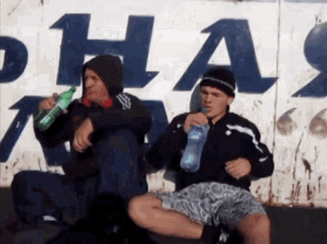 two young men are drinking from plastic bottles in front of a wall that says phas