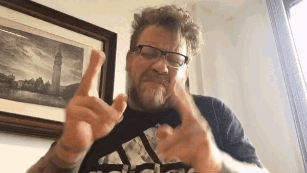 a man with glasses and a beard is wearing an adidas shirt and making a peace sign with his hands .