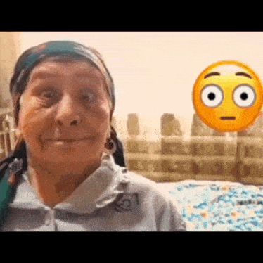 an elderly woman with a scarf around her head is making a funny face in front of a smiley face .