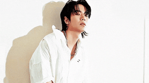 a young man wearing a white shirt and a chain around his neck looks at the camera