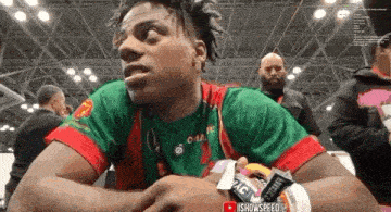 a man in a green and red shirt is sitting in front of a crowd of people .