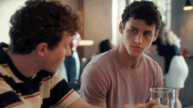 two young men are sitting at a table talking to each other in a restaurant .