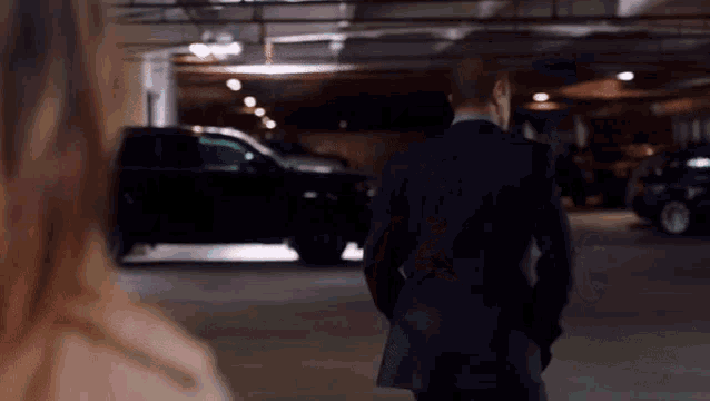 a man in a suit and a woman in a trench coat are standing in a parking garage .