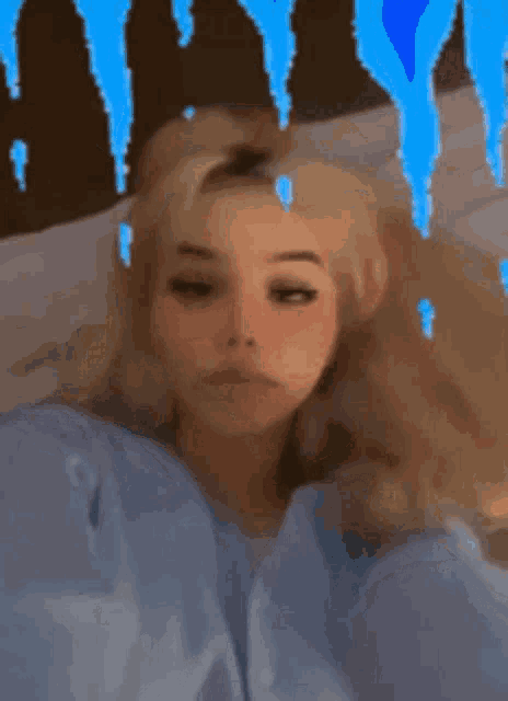 a girl with blonde hair and blue eyes is laying on a bed with a blue background .