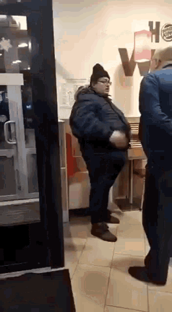 a man in a jacket and hat is standing in a restaurant .