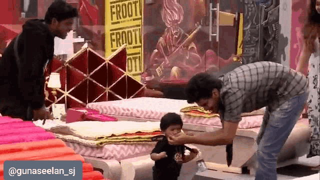 a man feeds a baby in front of a sign that says frooti
