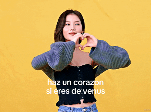 a woman making a heart shape with her hands in front of a yellow background