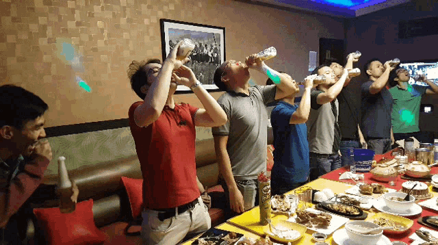 a group of men are drinking from bottles in front of a table full of food