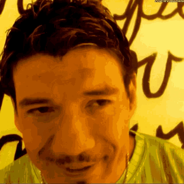 a man in a green shirt is smiling in front of a wall that says " you " on it