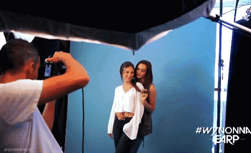 a man is taking a picture of two women in front of a blue wall with #wynonna earp written on the bottom