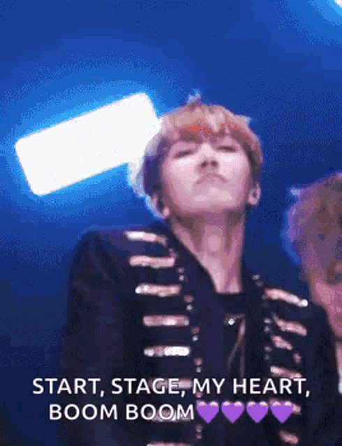 a man in a black jacket is standing on a stage and says `` start , stage my heart , boom boom '' .