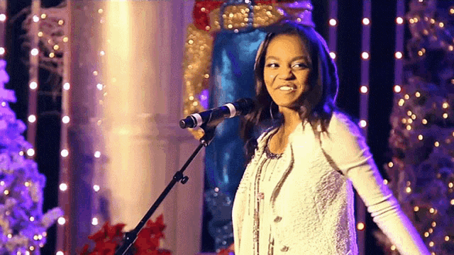 a woman is singing into a microphone in front of a christmas tree