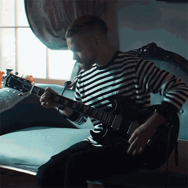 a man in a black and white striped shirt is playing a gibson guitar