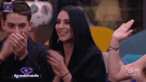 a woman applauds in front of a sign that says grande fratello on it