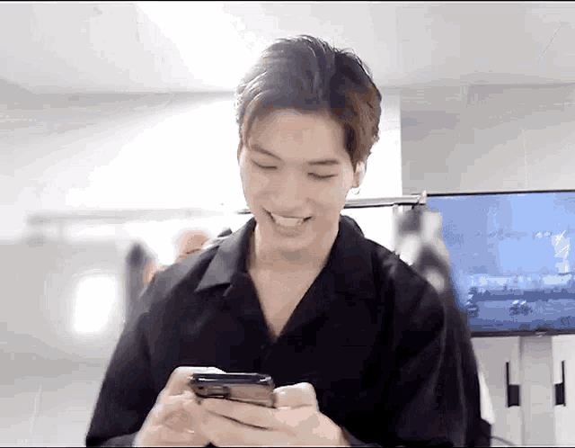 a young man in a black shirt is smiling while holding a cell phone in his hands .